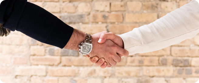 Two people shaking hands against a brick wall at the Cross Street office in Chicago.