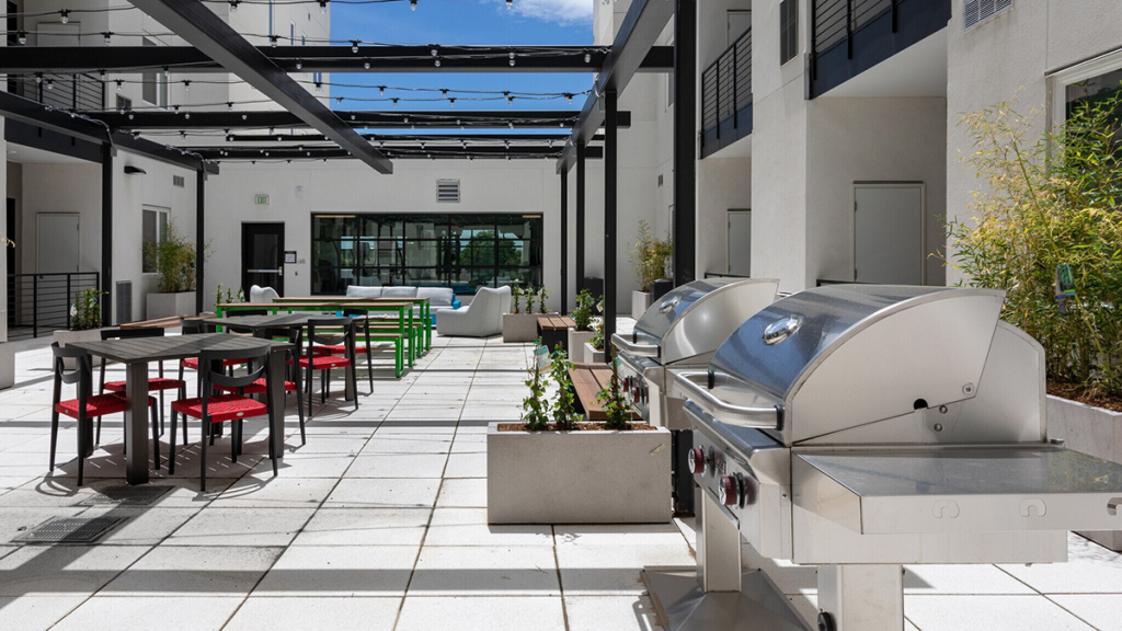 An amenity space at POP Denver, new apartments in Santa Fe Art District in Denver. The photo depicts a community courtyard and outdoor grills.